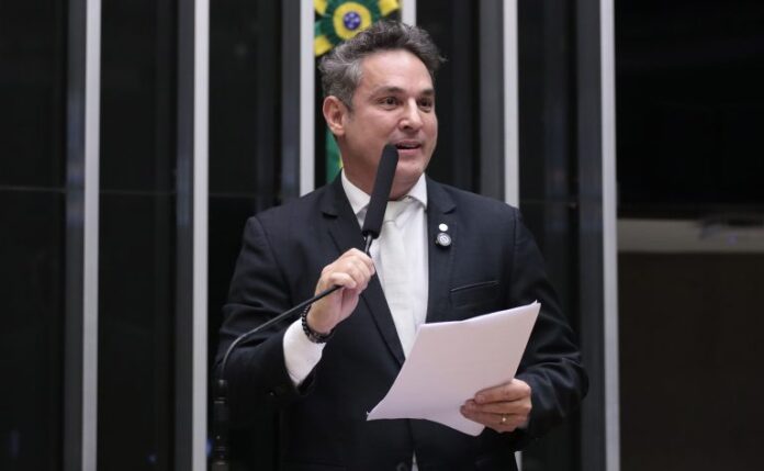 Comissão aprova regras mais duras para crimes graves, incluindo restrição Deputado Zucco fala ao microfone. Ele é um homem claro, com cabelo curto e escuro. Veste um terno azul-marinho e segura um papel