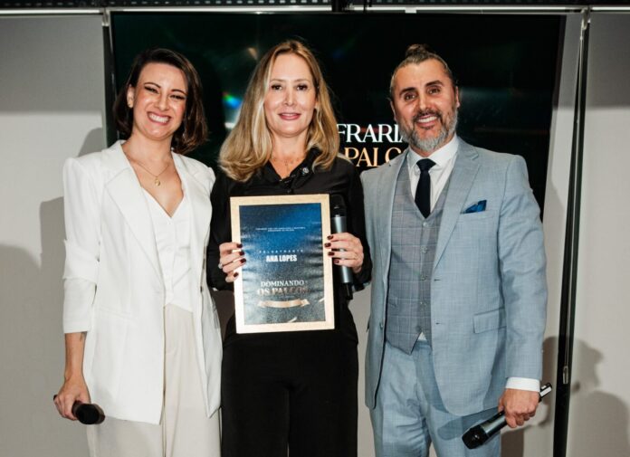 1 Ana Lopes segura placa de reconhecimento durante evento da Confraria dos Palcos ao lado de Bruna Grah e Fernando Freitas em palco de premiação.