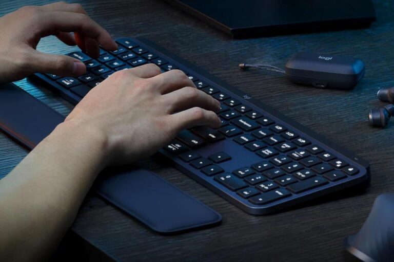 zoom-nas-mãos-de-pessoa-digitando-no-Teclado-sem-fio-Logitech-MX-Keys-S-com-teclas-iluminadas-em-ambiente-escuro