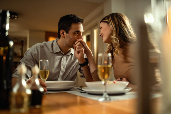 Young romantic man kissing girlfriend's hand during dinner at di magnific.com